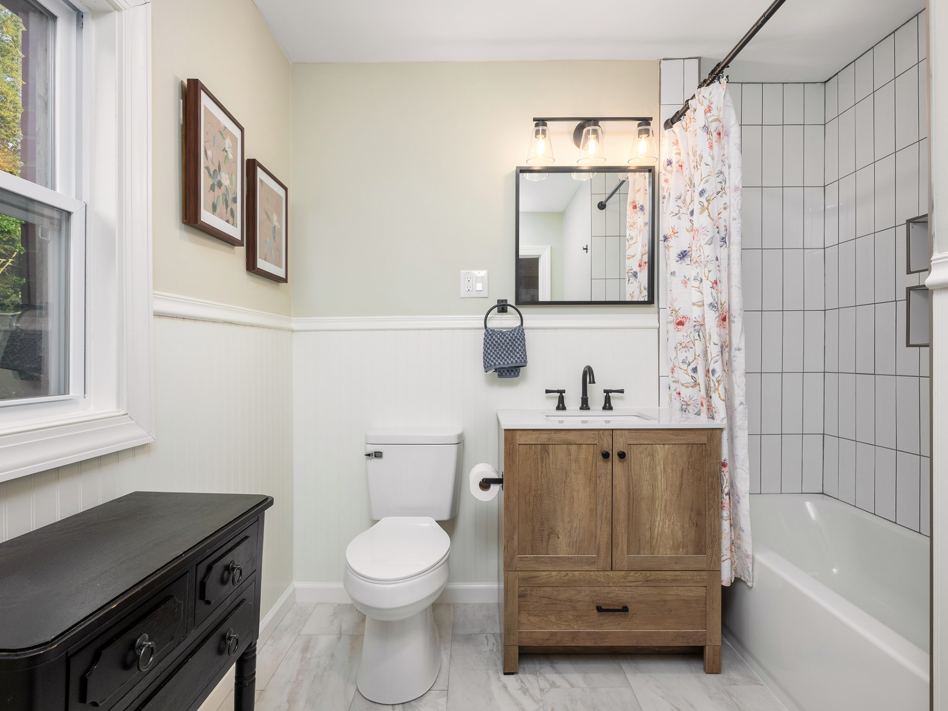 Bathroom with wood vanity, matte black fixtures, beadboard wainscoting and a tiled tub and shower
